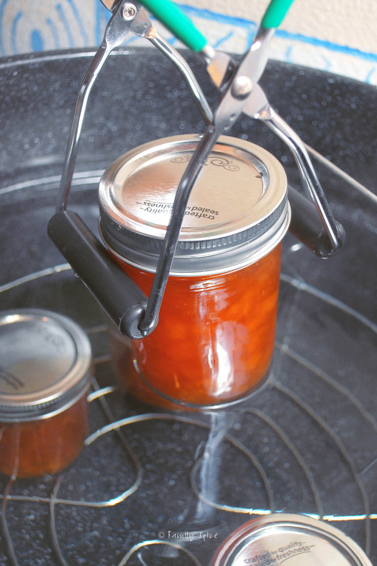 Placing a mason jar with peach jam into a pot with hot water to can.
