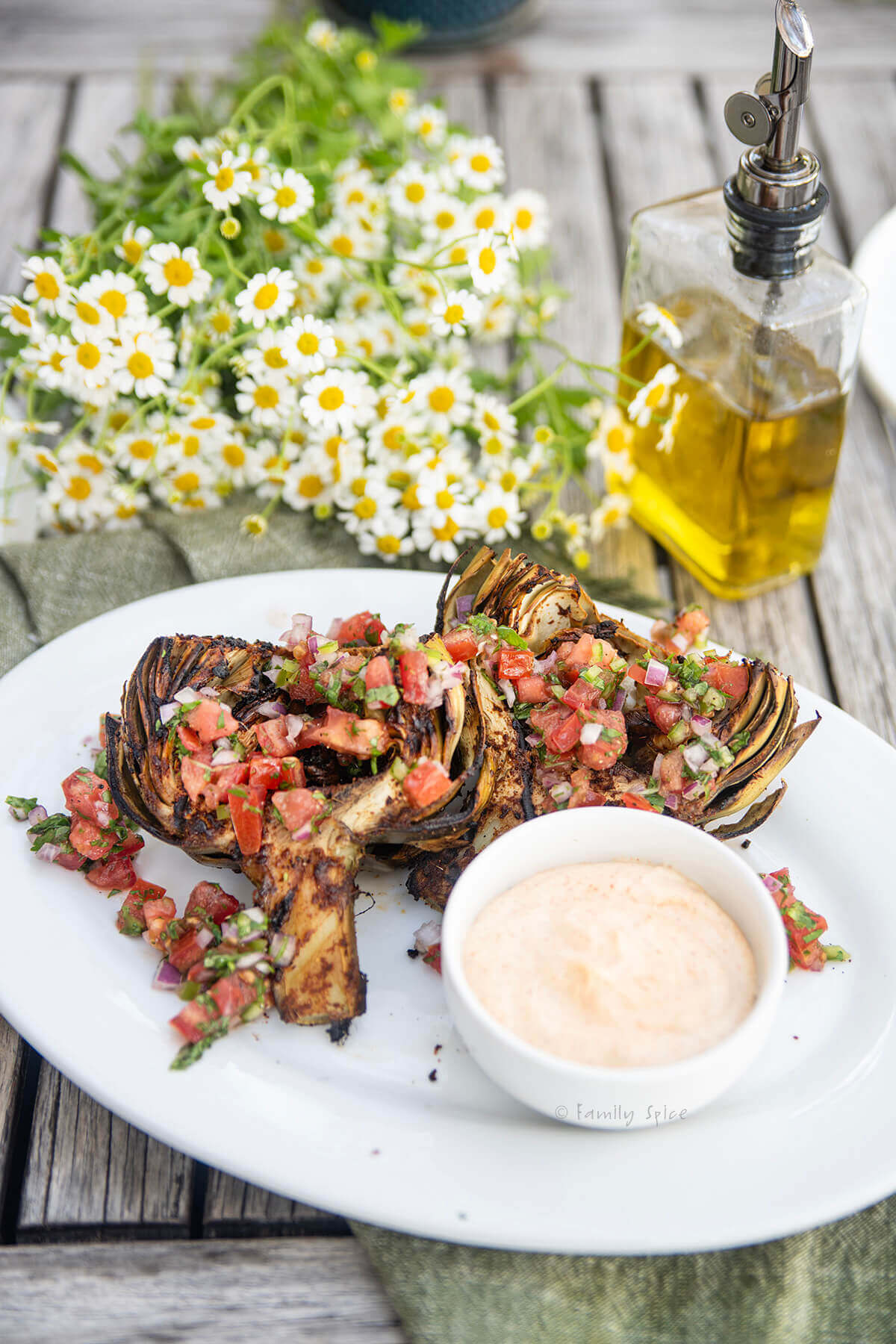 A white plate with a chile lime grilled artichoke garnished with pico de gallo and served with a chile mayo.