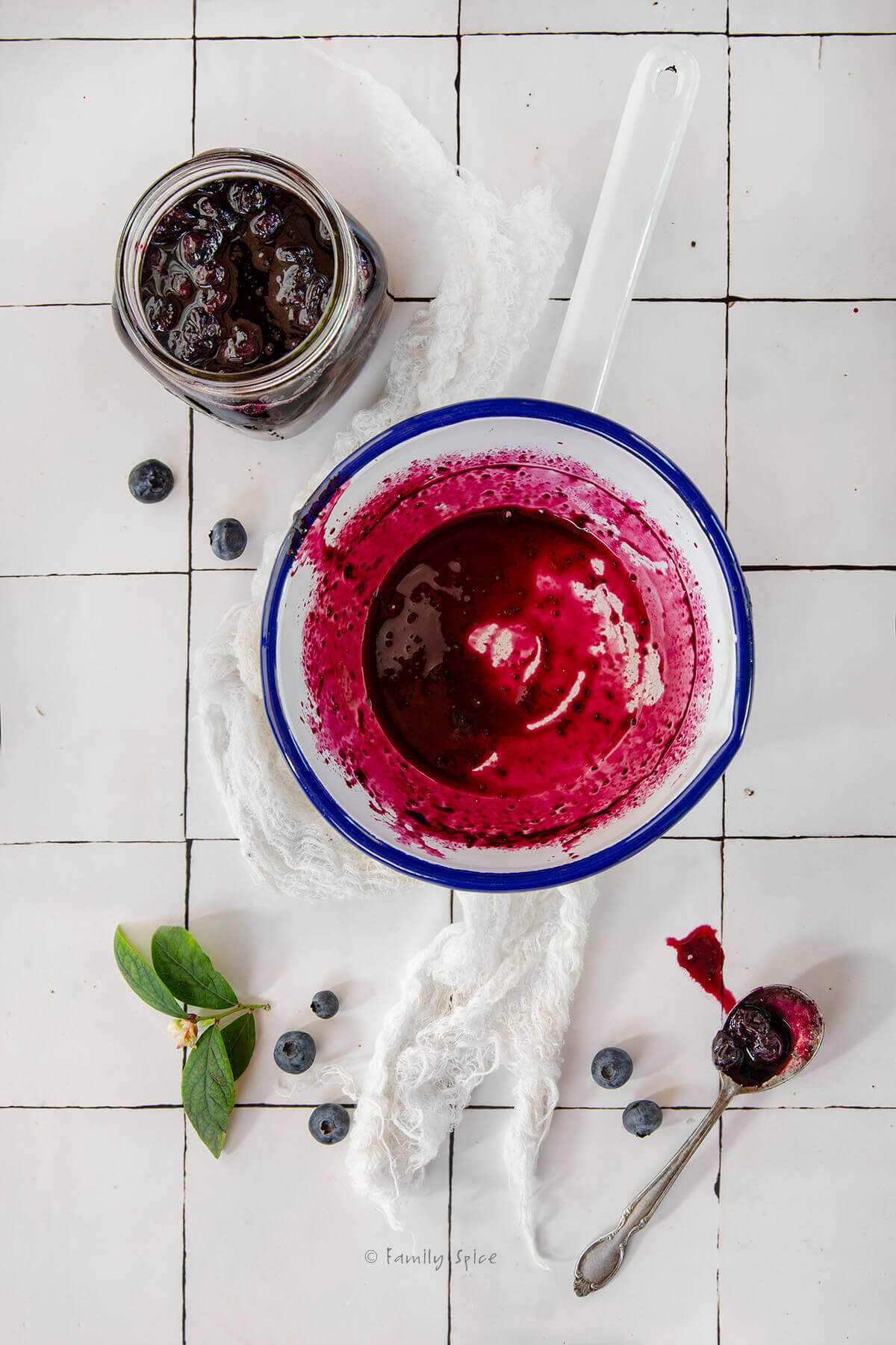 Top view of a mason jar with homemade blueberry preserves in it along with an enamel pot with blueberry syrup in it