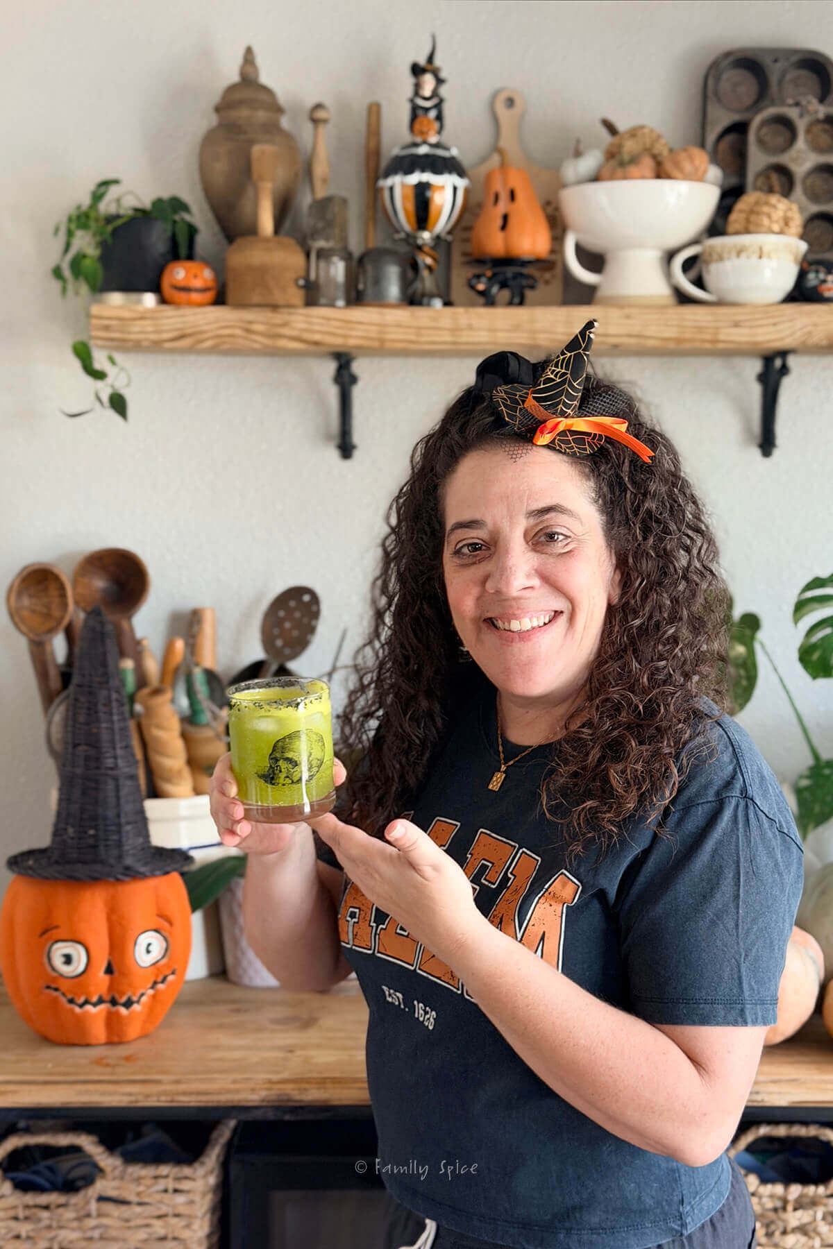 Laura Bashar with a mini witch hat in her hair holding a kiwano halloween margarita.