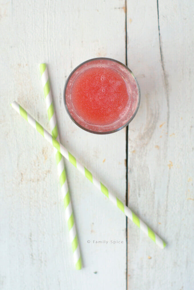 Top view of a glass of watermelon juice with two green striped straws next to it