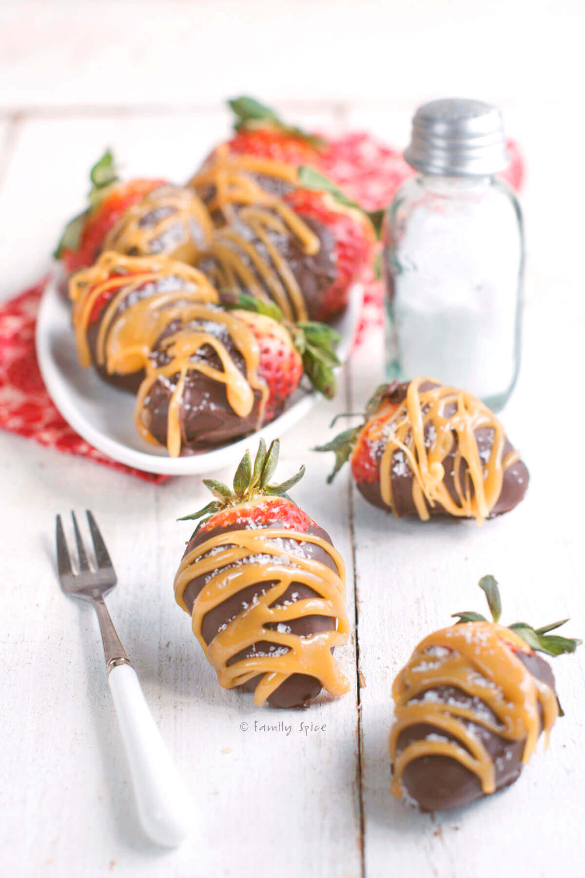 Side view of a white plate with chocolate and caramel covered strawberries.
