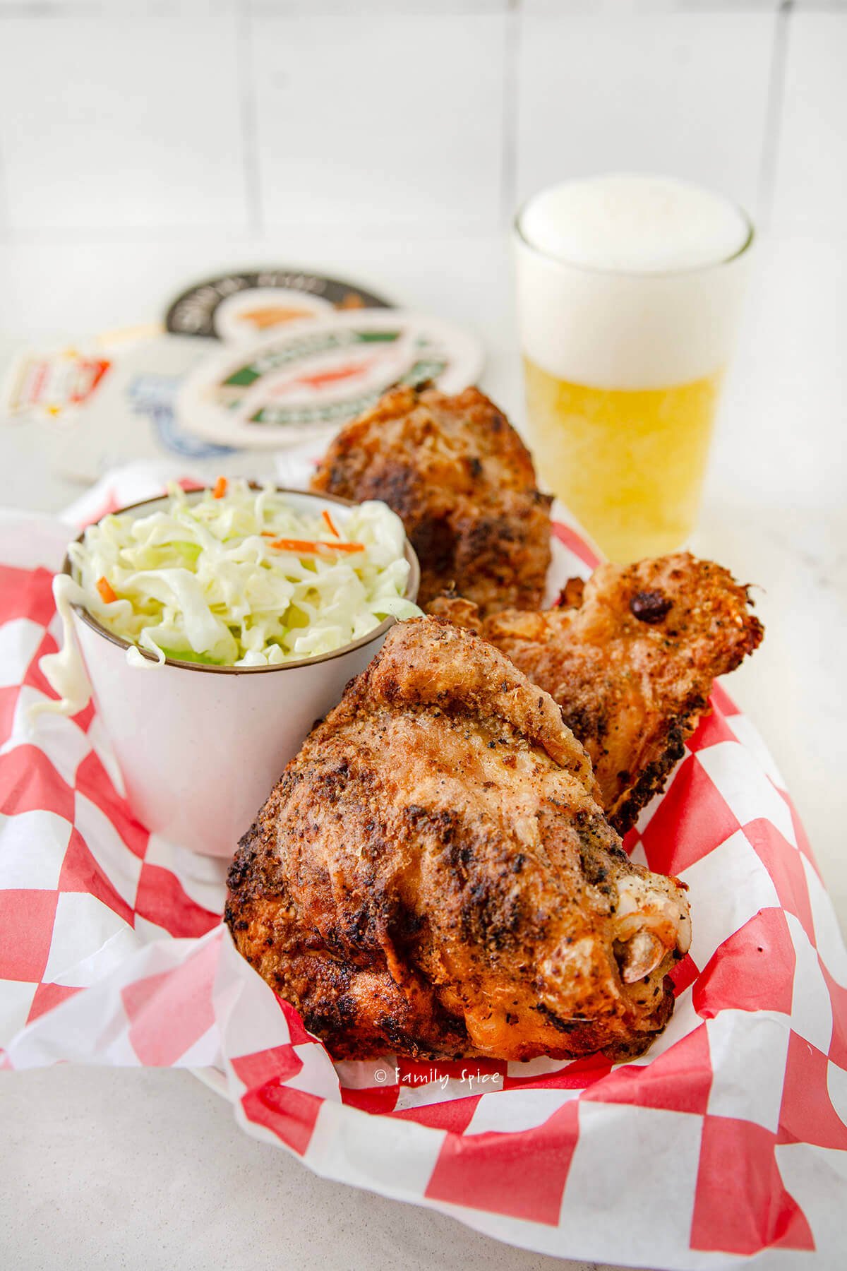Several oven fried chicken thighs in a food basket with a side of slaw and beer behind it.