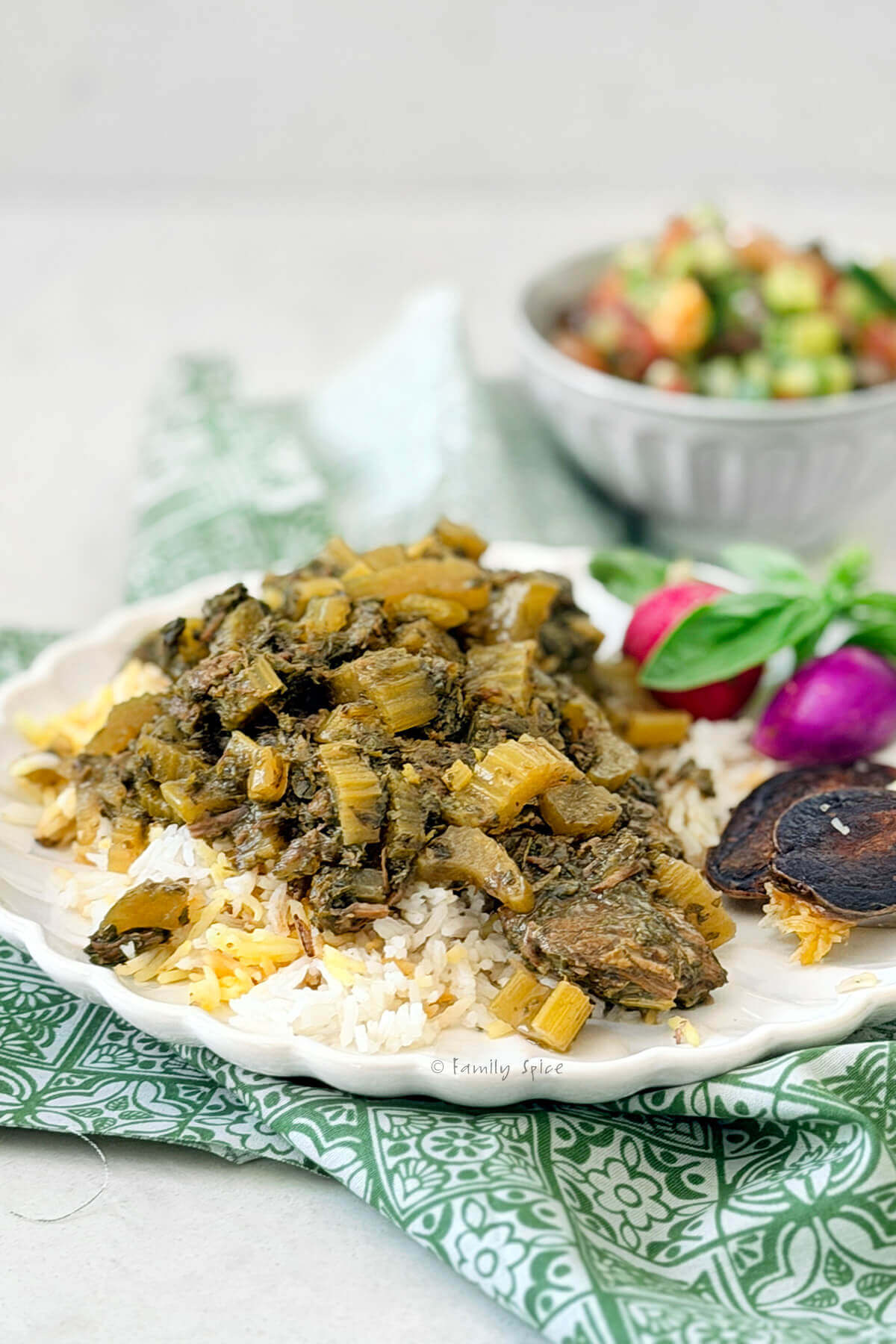 Side view of a plate with Persian rice and celery stew (khoresh karafs) with radishes, herbs and shirazi salad.