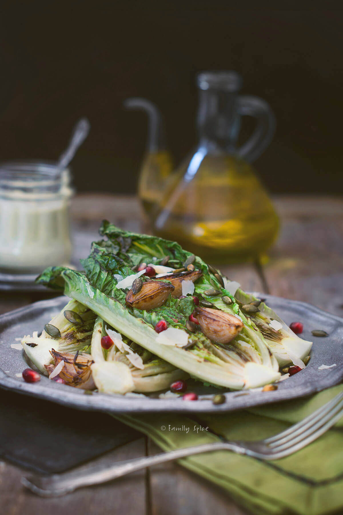 A pewter plate with grilled romaine lettuce topped with roasted shallots and pomegranate arils