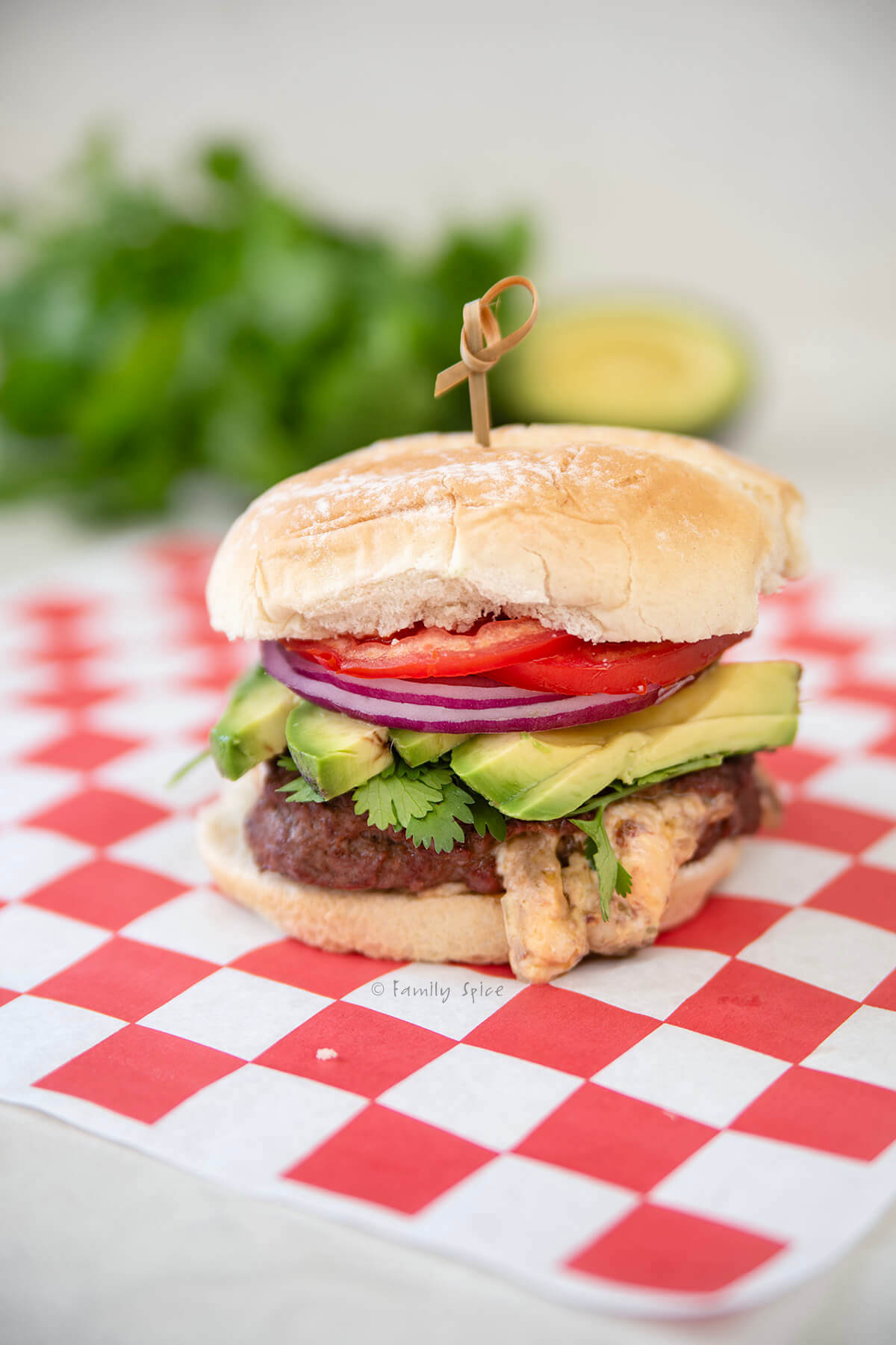 Closeup of a queso stuffed burger on a red and white checkered paper.