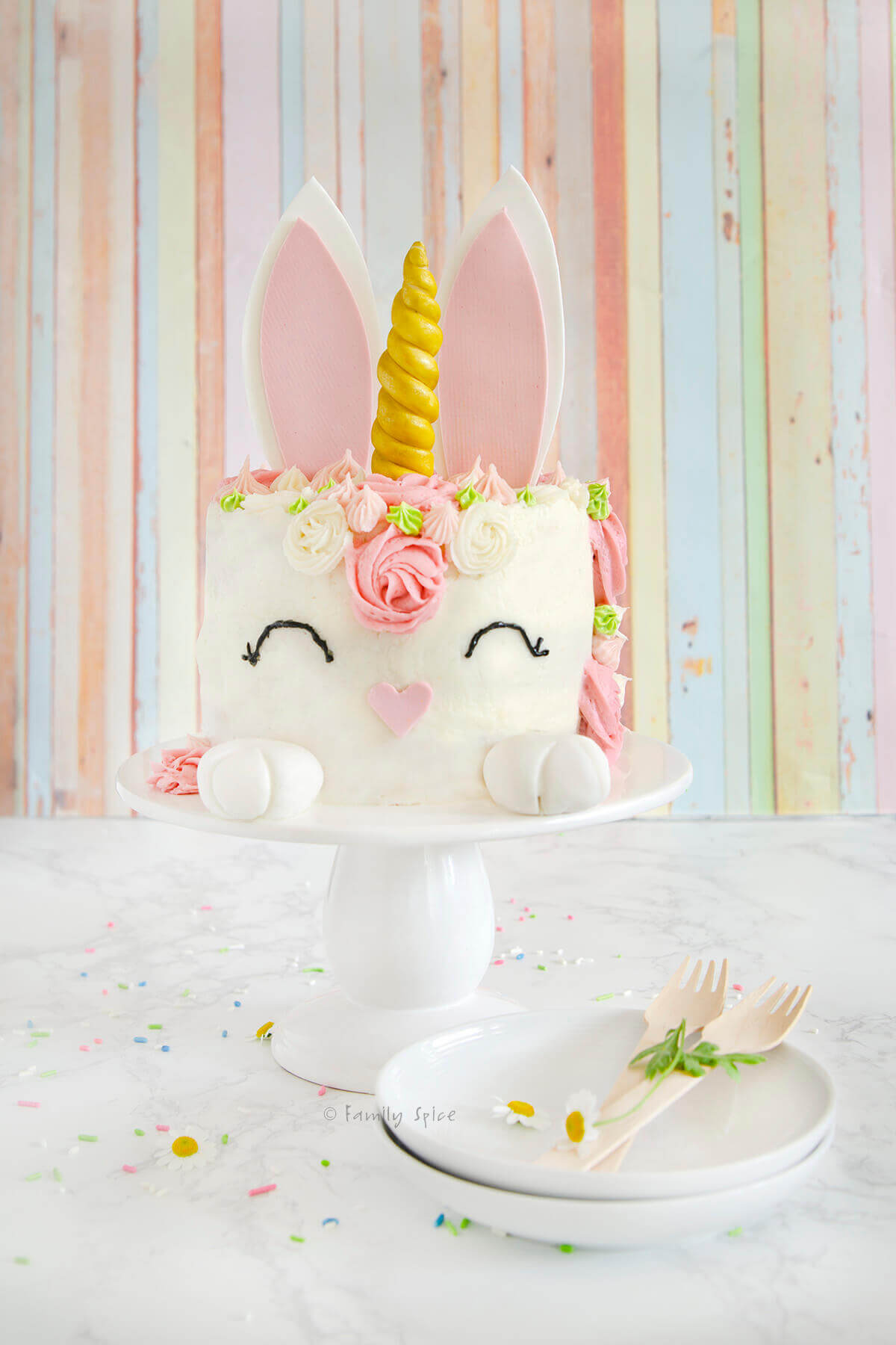 A pastel decorated bunny unicorn cake on a white pedestal.