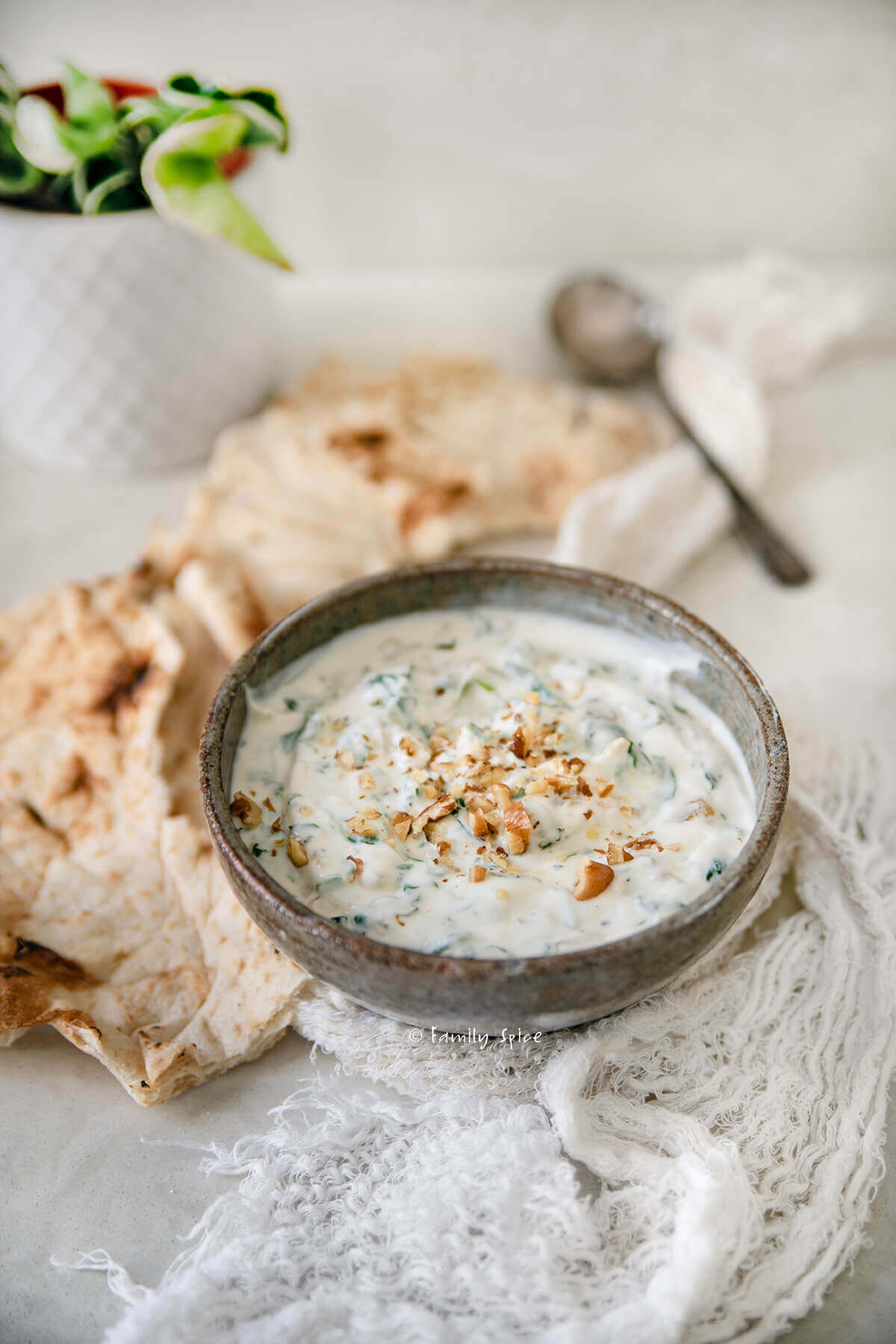 Side view of a bowl with spinach borani in it and lavash bread around it.
