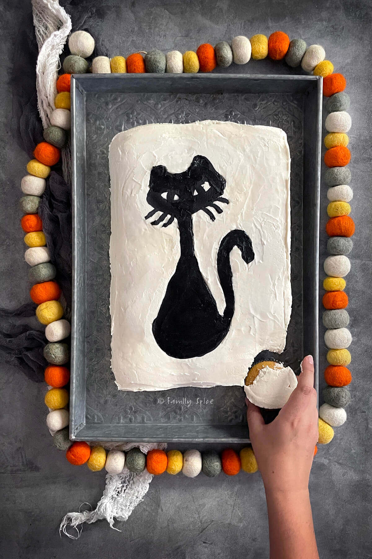 A hand pulling out one cupcake from a halloween pull apart cupcake cake frosted white with a black cat.