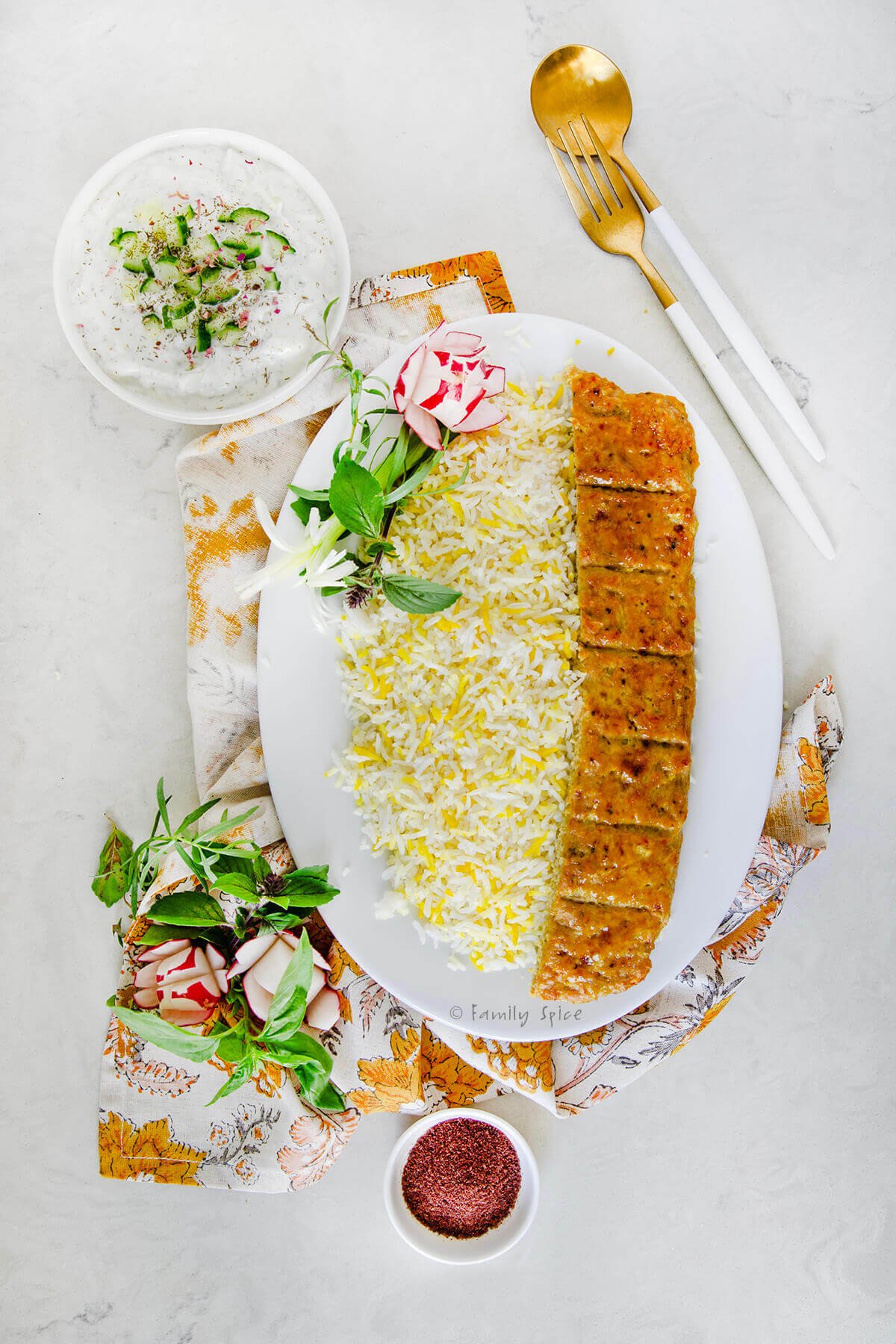 Top view of a plate of rice with chicken koobideh kabob along with yogurt, herbs and radishes around it.