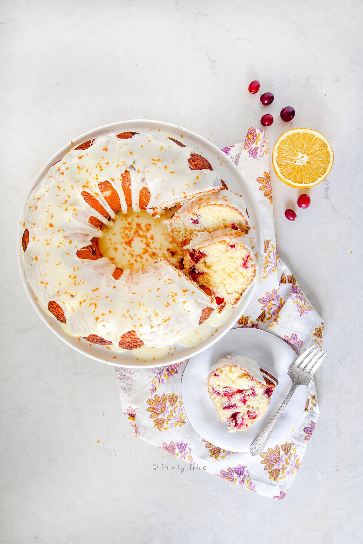 Top view of a slice of orange cranberry olive oil cake on a plate with the rest of the cake next to it.