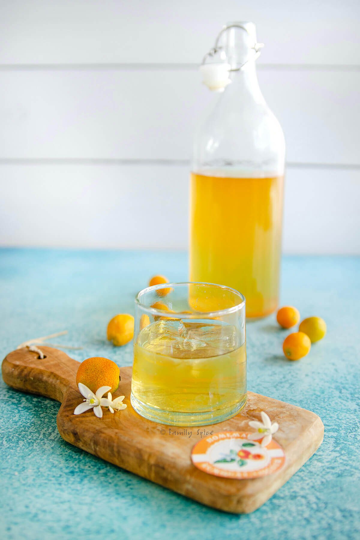 A short glass with kumquat liqueur sitting on a small cutting board with a bottle with more liqueur behind it.