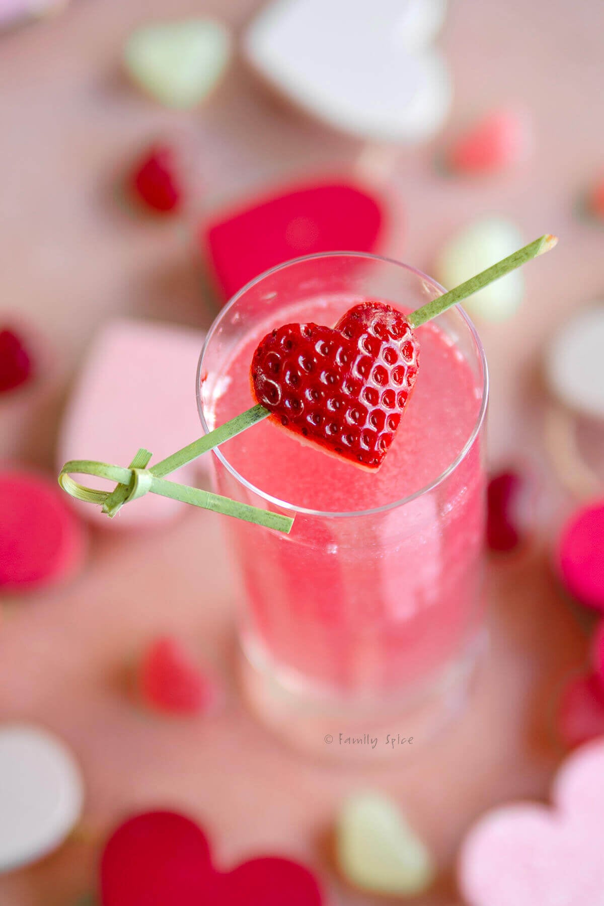 Top view of a champagne flute filled with shimmering pink mimosa garnished with a heart shaped strawberry on a toothpick.