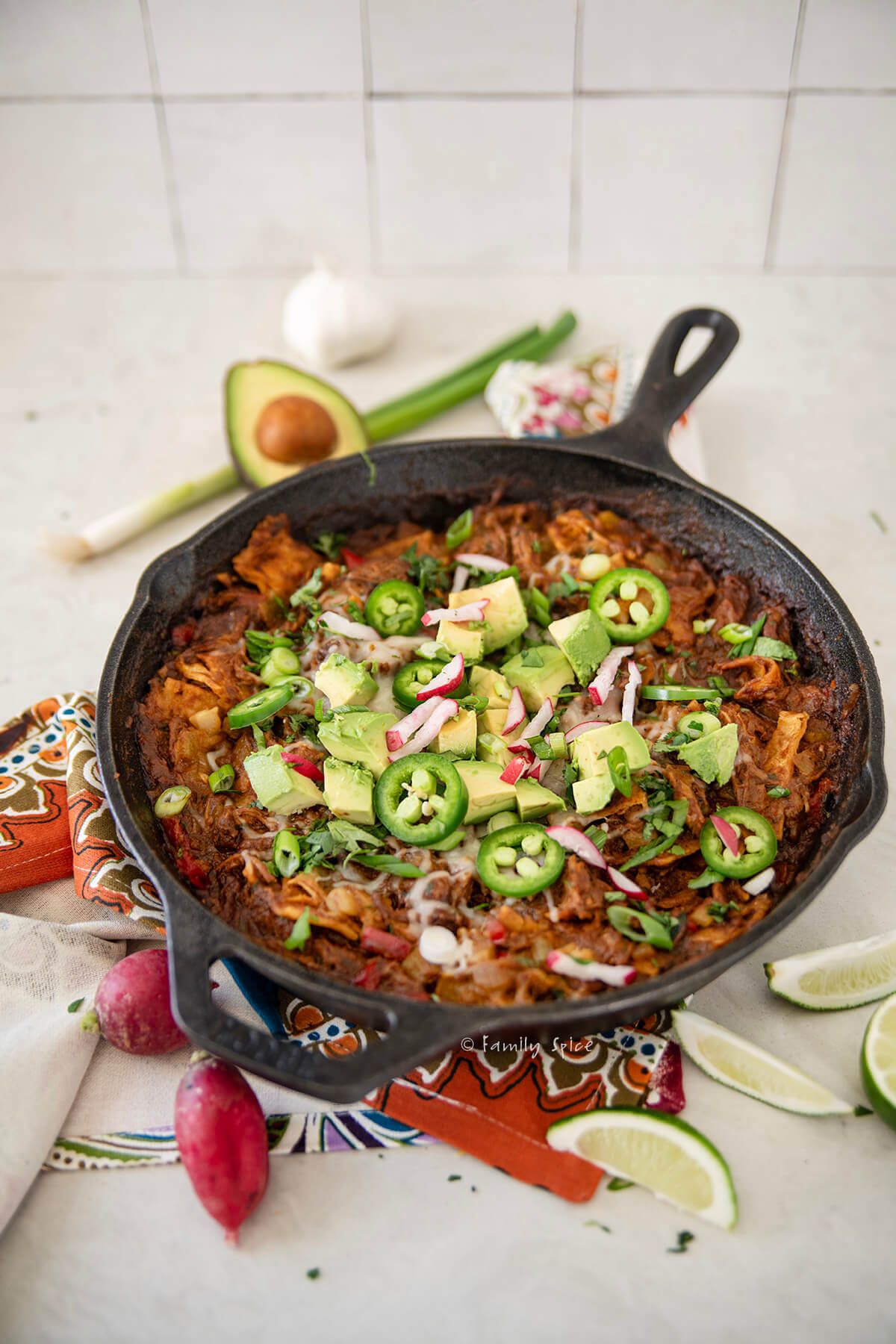 Side view of pulled pork enchilada skillet with various ingredients around it.