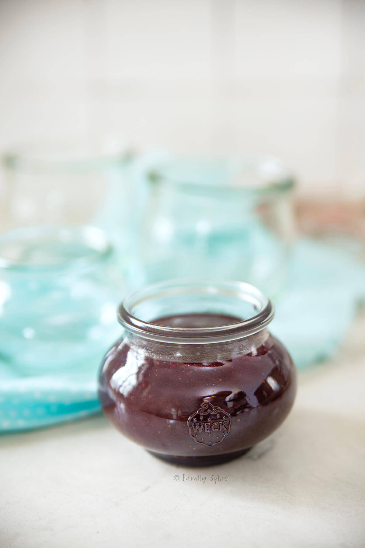 Closeup of a glass jar with mixed fruit jam in it and empty jars behind it.