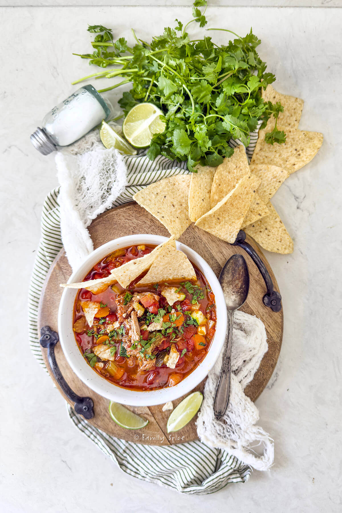 Top view of a white bowl with pulled pork tortilla soup and ingredients behind it.