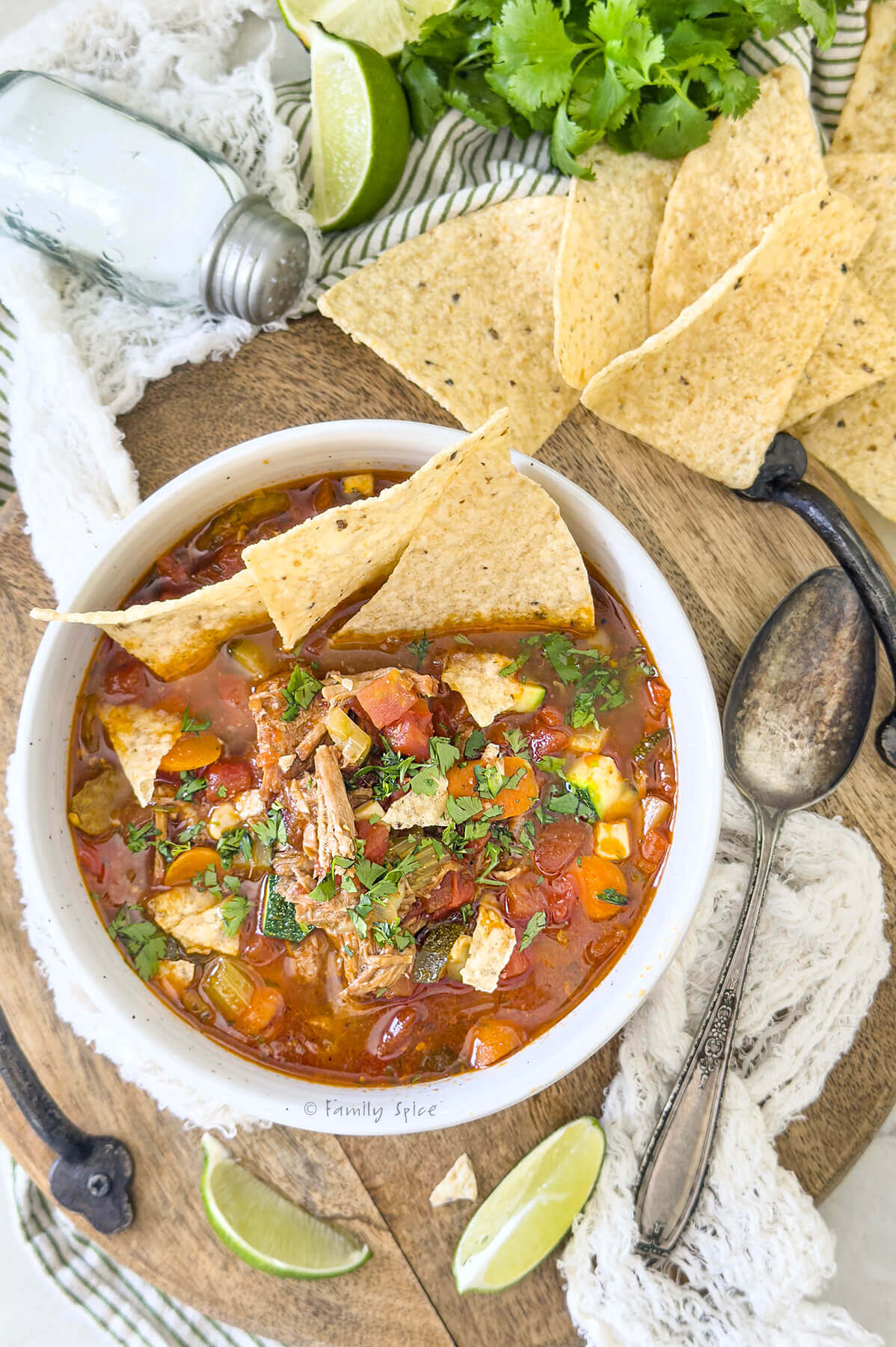Closeup top view of a white bowl with pulled pork tortilla soup and ingredients behind it.