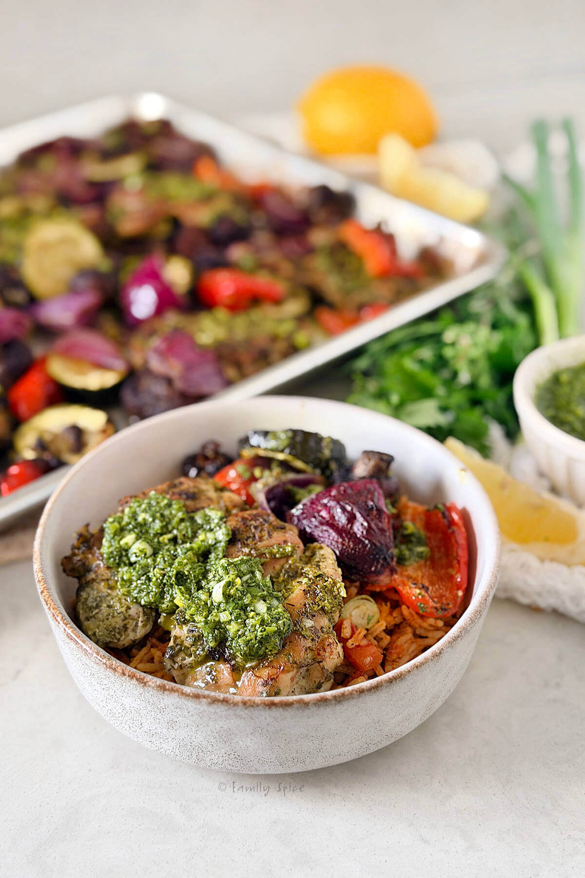 Closeup of a bowl with chicken chimichurri with vegetables in it with the remaining on a sheet pan behind it.