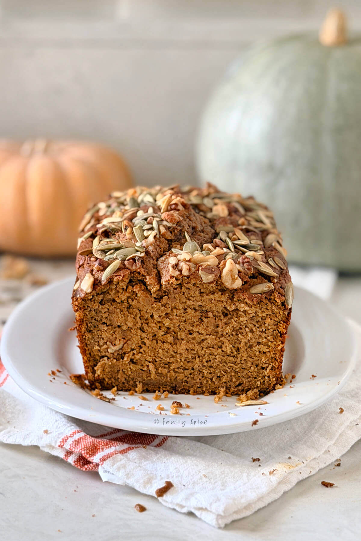 Closeup of a loaf of olive oil pumpkin bread sliced open and two pumpkins behind it.