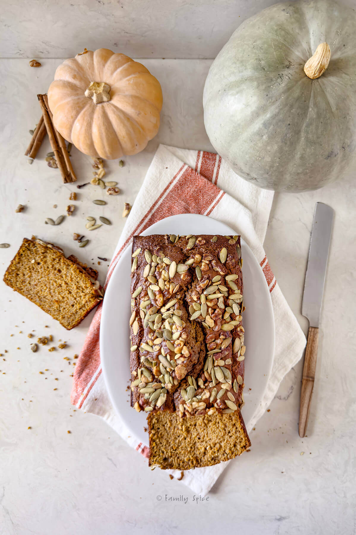 Top view of a loaf of olive oil pumpkin bread with a couple slices cut off and two pumpkins next to it.