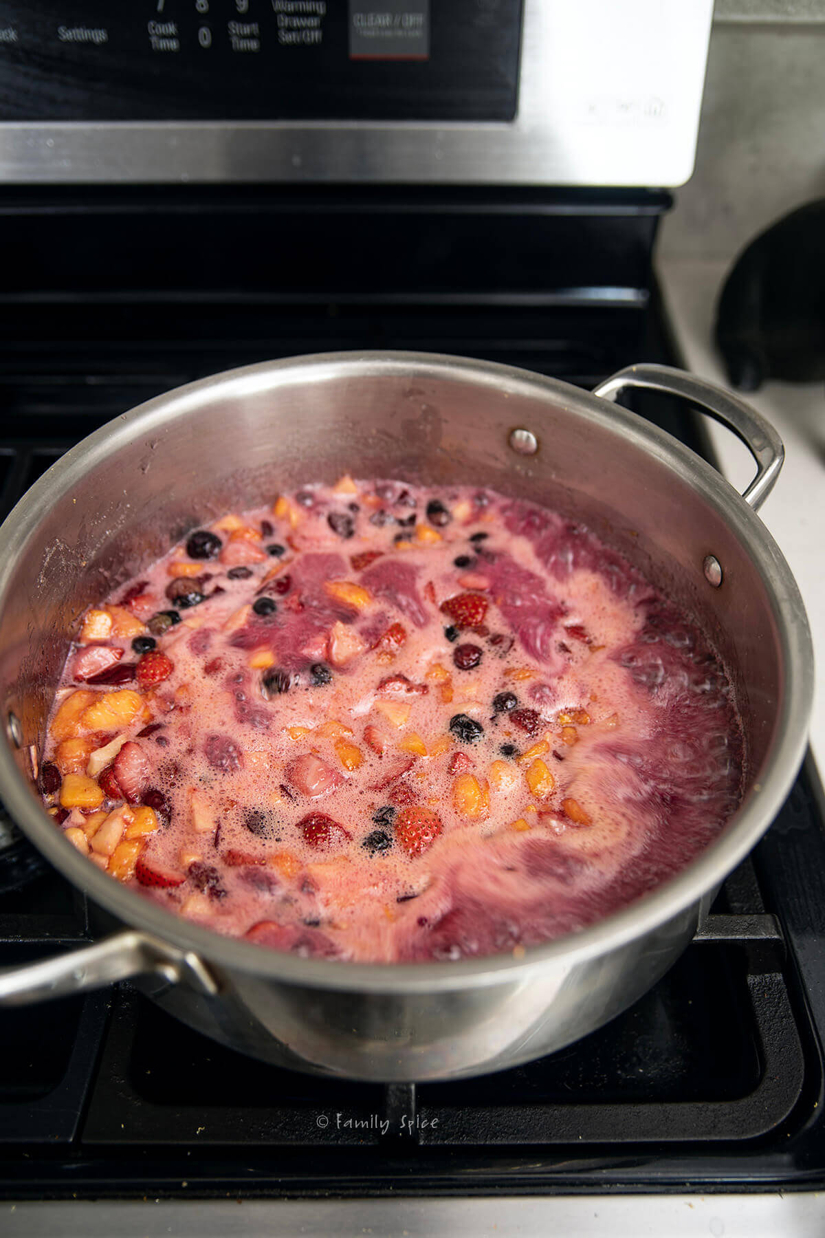 A pot with fruits boiling in it to make mixed fruit jam.