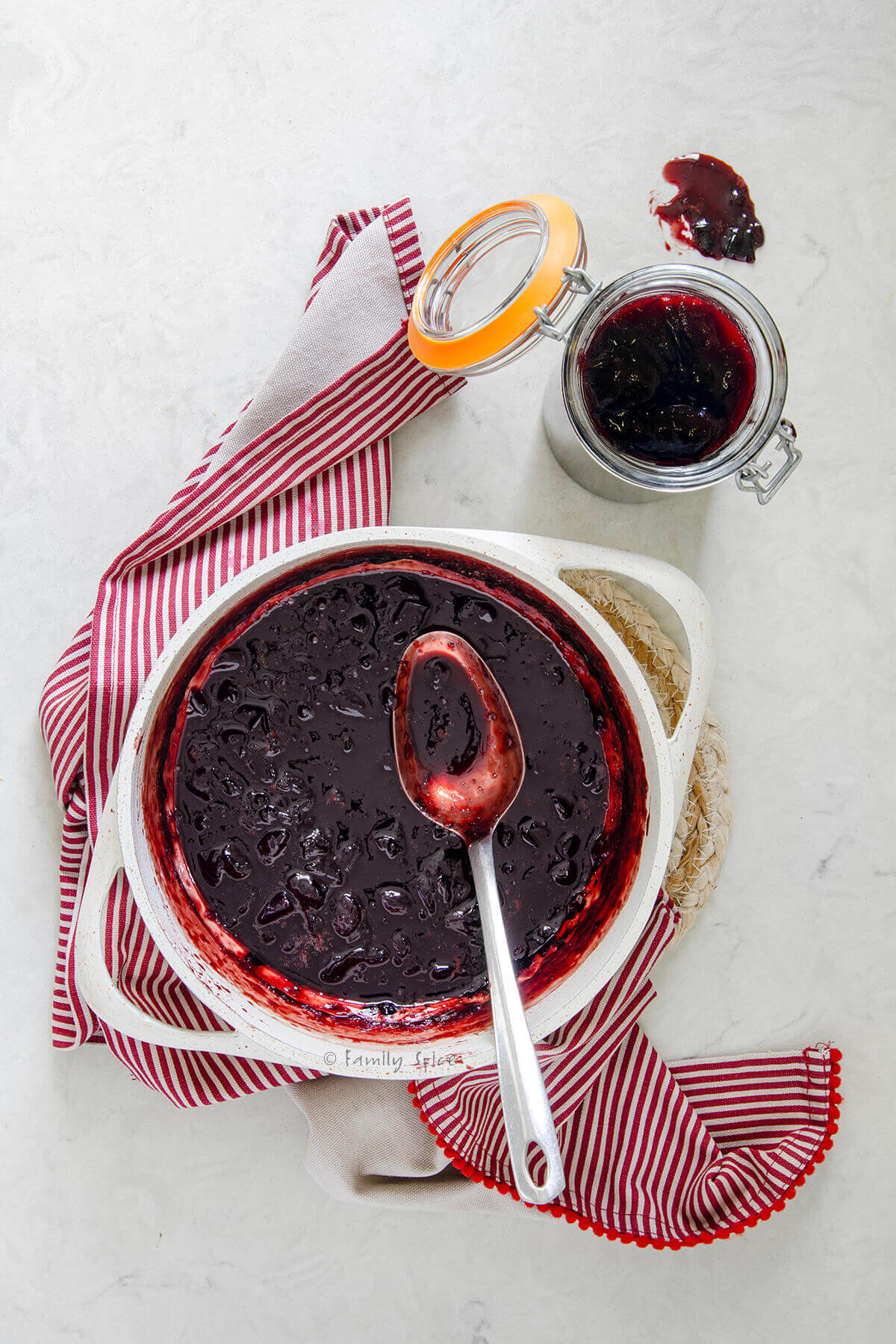 Top view of a pot with hot plum jam in it and a jar of plum jam next to it.