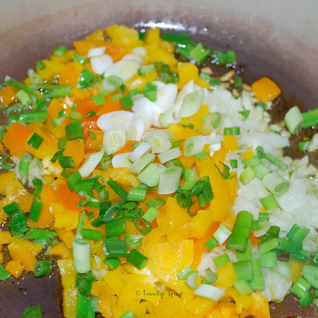 Diced onions, yellow bell peppers and green onions sautéeing in a pot