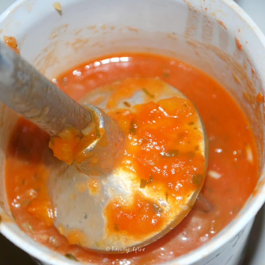 An immersion blender mixing up a tomato mixture in a plastic cup
