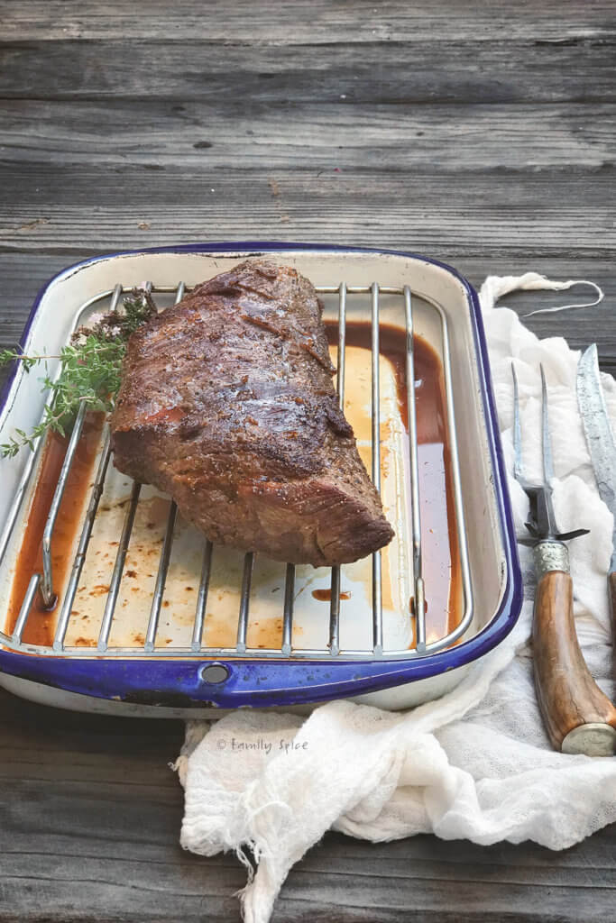 Side view of an oven roasted tri tip on a white enamel roasting pan
