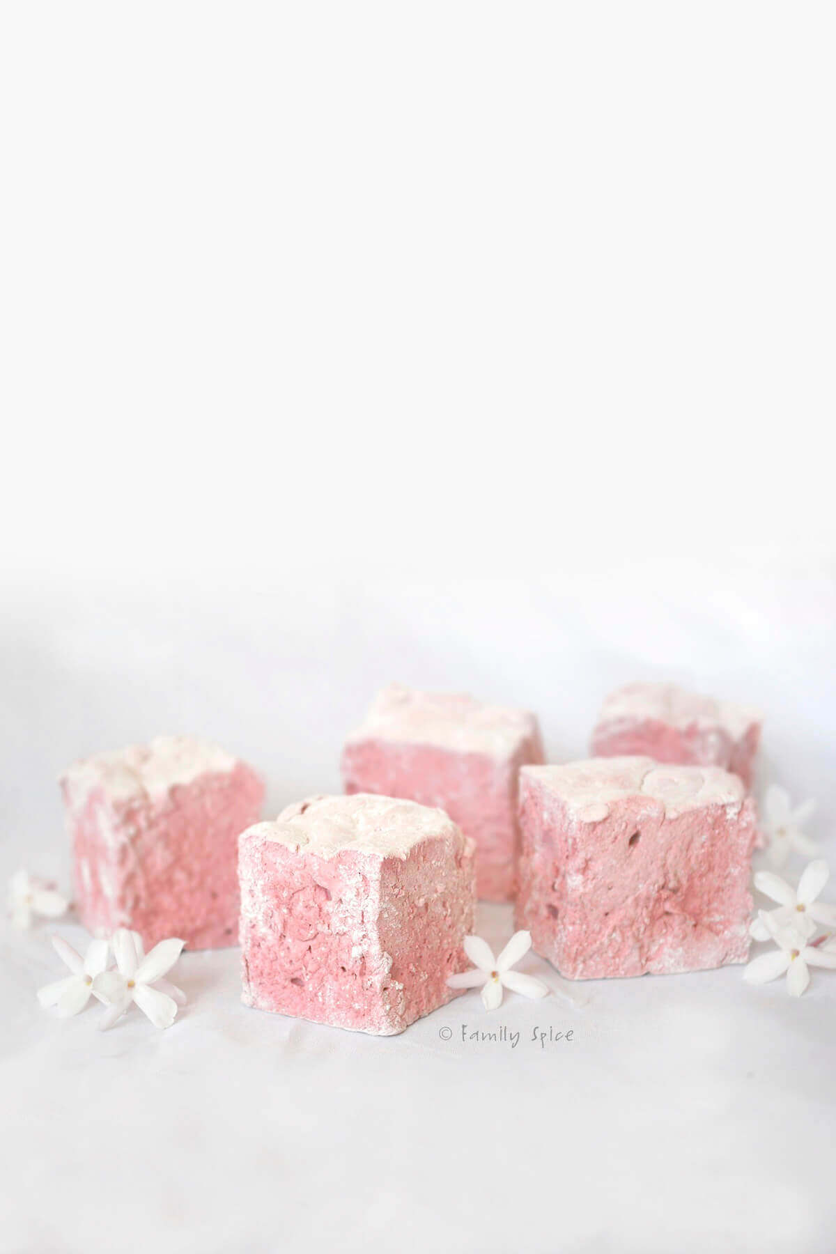 Light pink pomegranate marshmallow cubes on white background with little white flowers