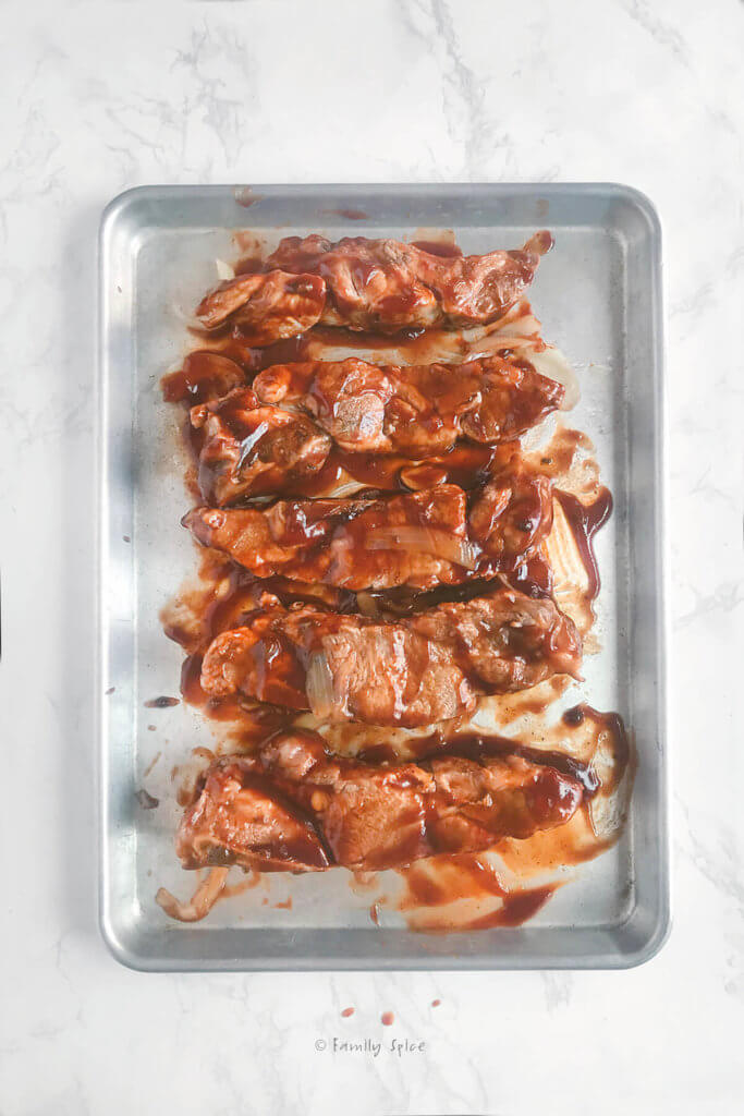 Boiled pork country style ribs topped with barbecue sauce on a baking sheet ready to bake in the oven