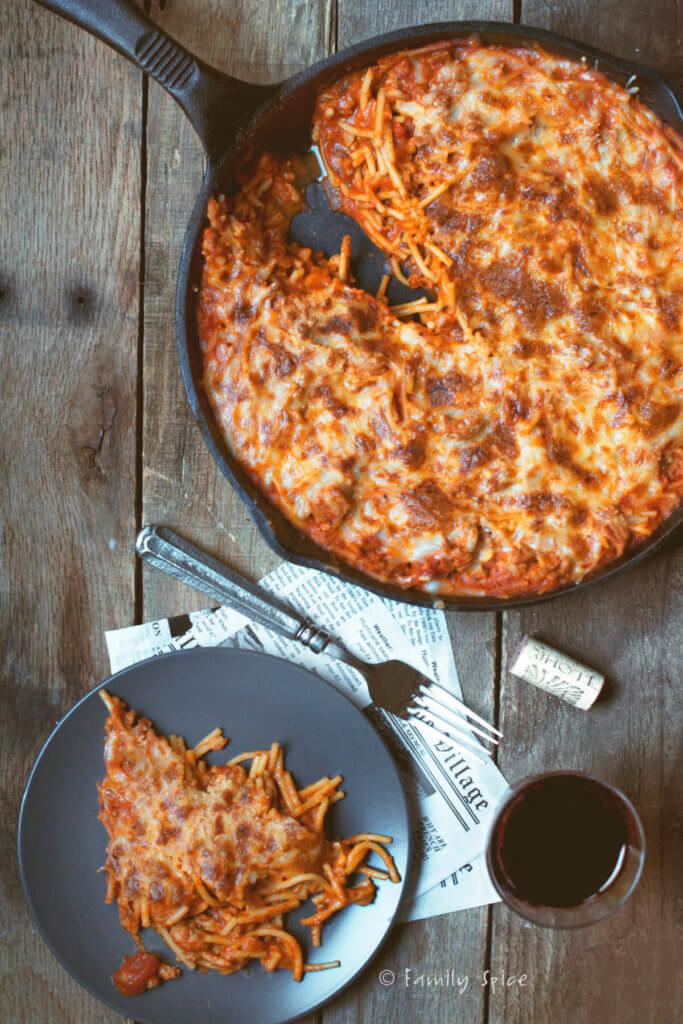 Overhead shot of a cast iron skillet with baked spaghetti and meat sauce and slice cut out