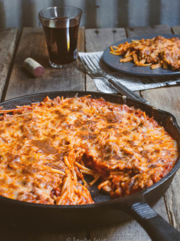 Side view of a cast iron skillet with baked spaghetti and meat sauce and slice cut out