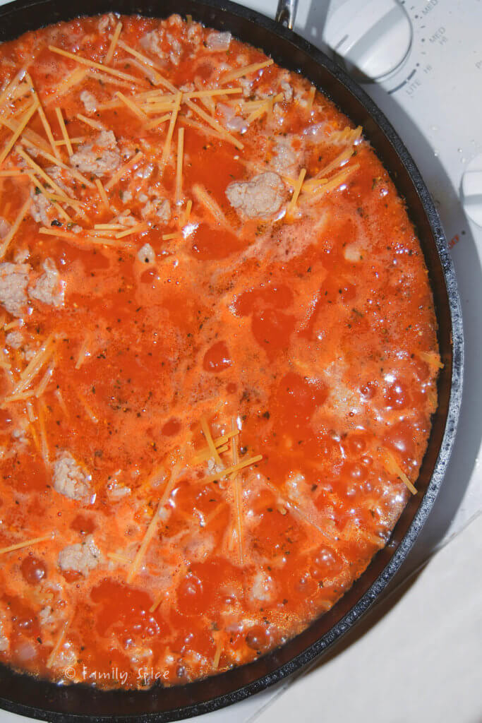 Adding broken spaghetti to tomato sauce with meat