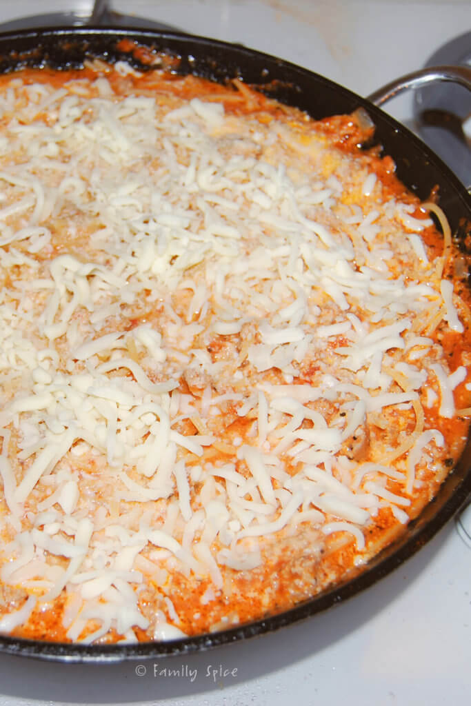Skillet with spaghetti dish topped with cheese and ready for the oven