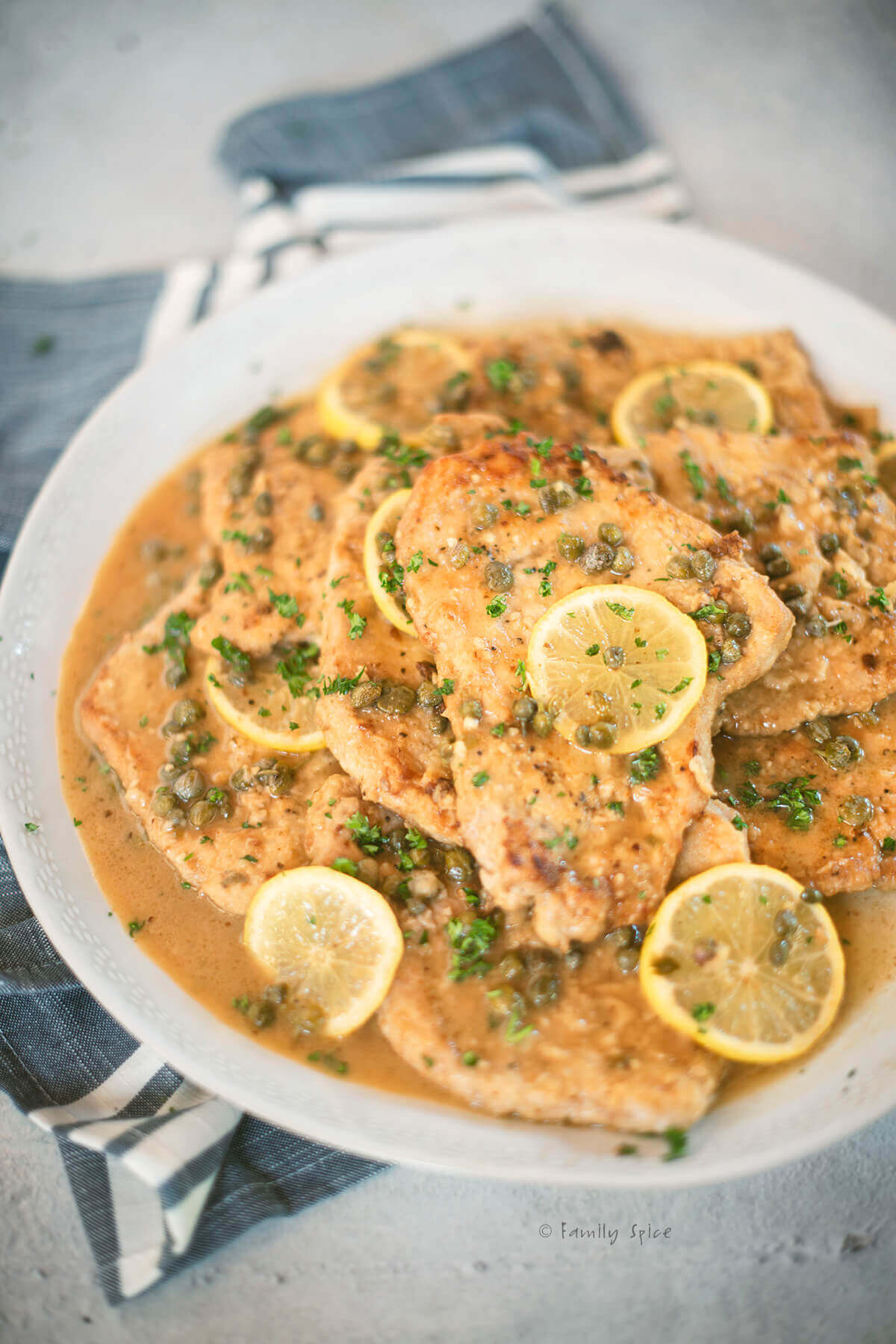 Closeup of a large round serving plate with pork piccata with lemon slices and capers