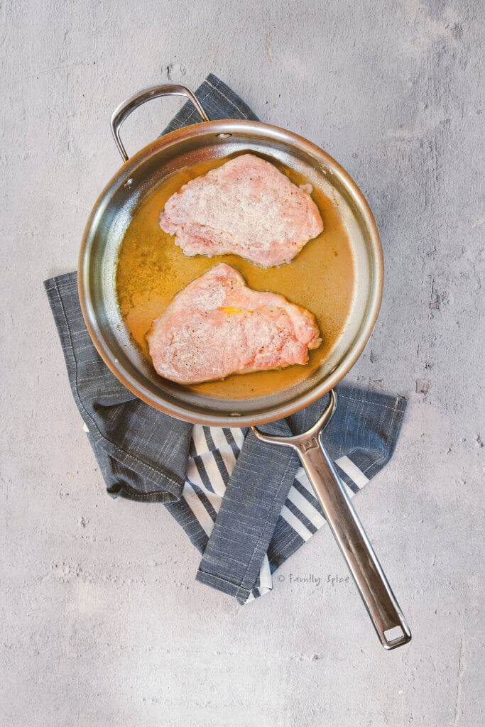 Browning two pork cutlets covered in flour in a large stainless frying pan