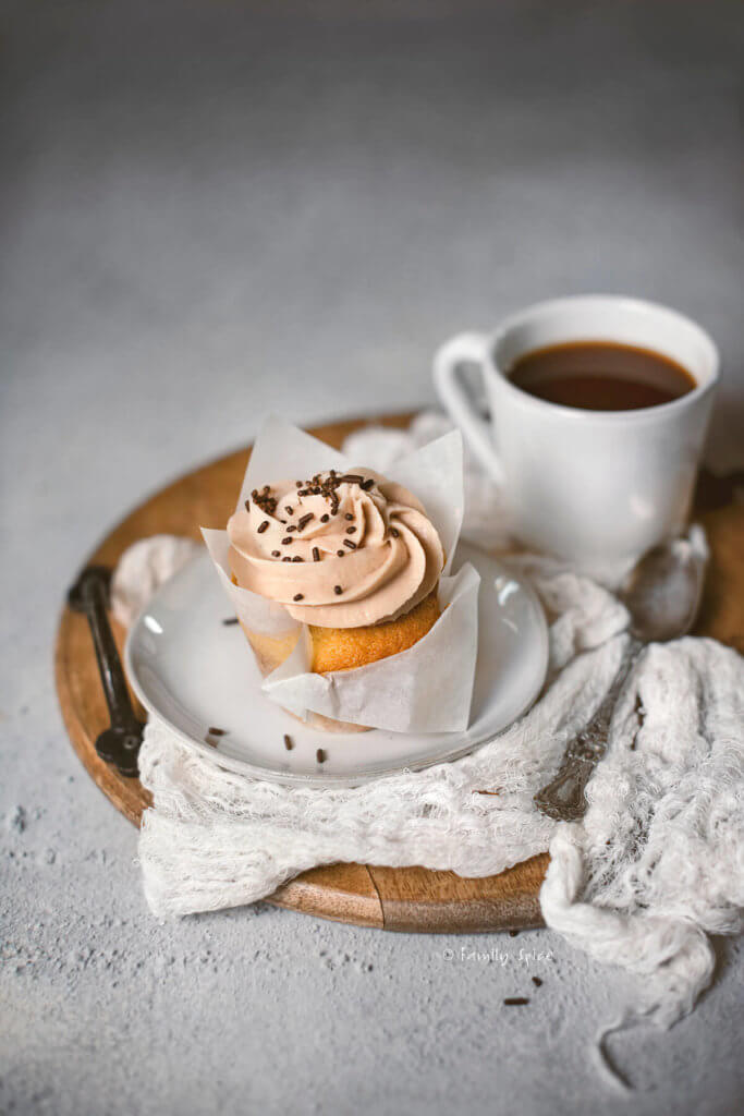 One Baileys cupcake on a small plate sitting on a wooden tray with a small mug of coffee next to it