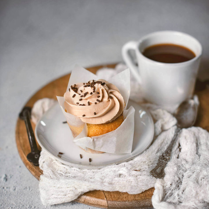 One Baileys cupcake on a small plate sitting on a wooden tray with a small mug of coffee next to it