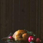 Roast turkey surrounded with pomegranates and eucalyptus branches on a dark and moody background
