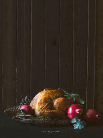 Roast turkey surrounded with pomegranates and eucalyptus branches on a dark and moody background