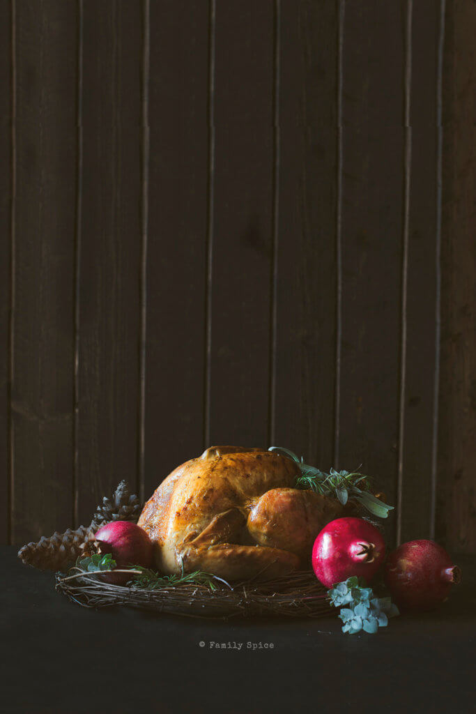 Roast turkey surrounded with pomegranates and eucalyptus branches on a dark and moody background