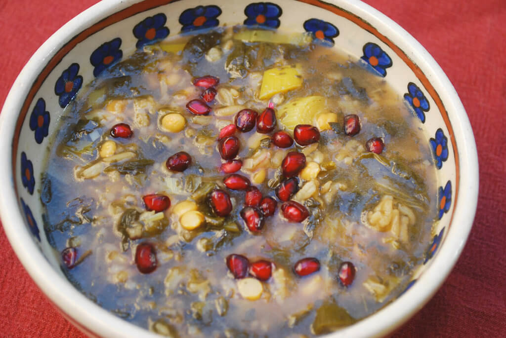 A bowl of ash anar (persian pomegranate soup) topped with pomegranate arils
