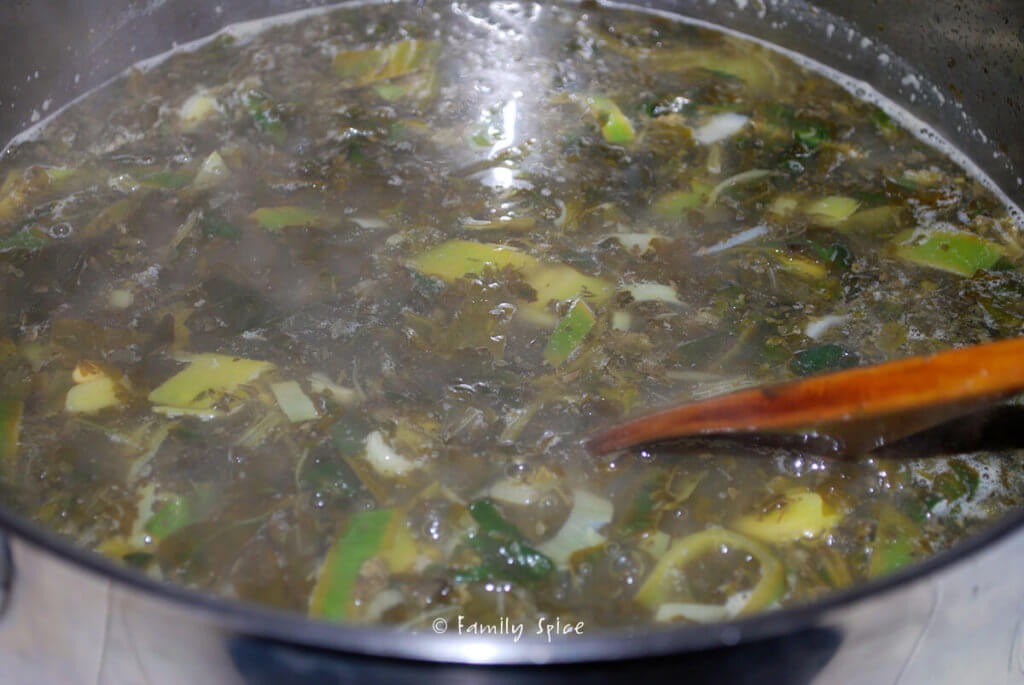 Adding broth in a pot with fresh herbs for soup