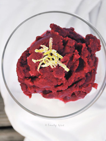 A glass bowl with pomegranate granita topped with lemon peel