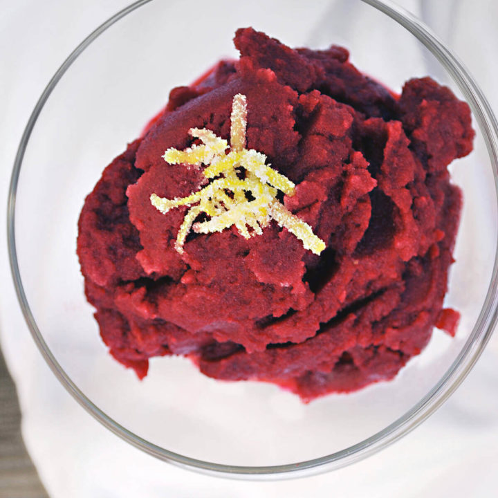 A glass bowl with pomegranate granita topped with lemon peel