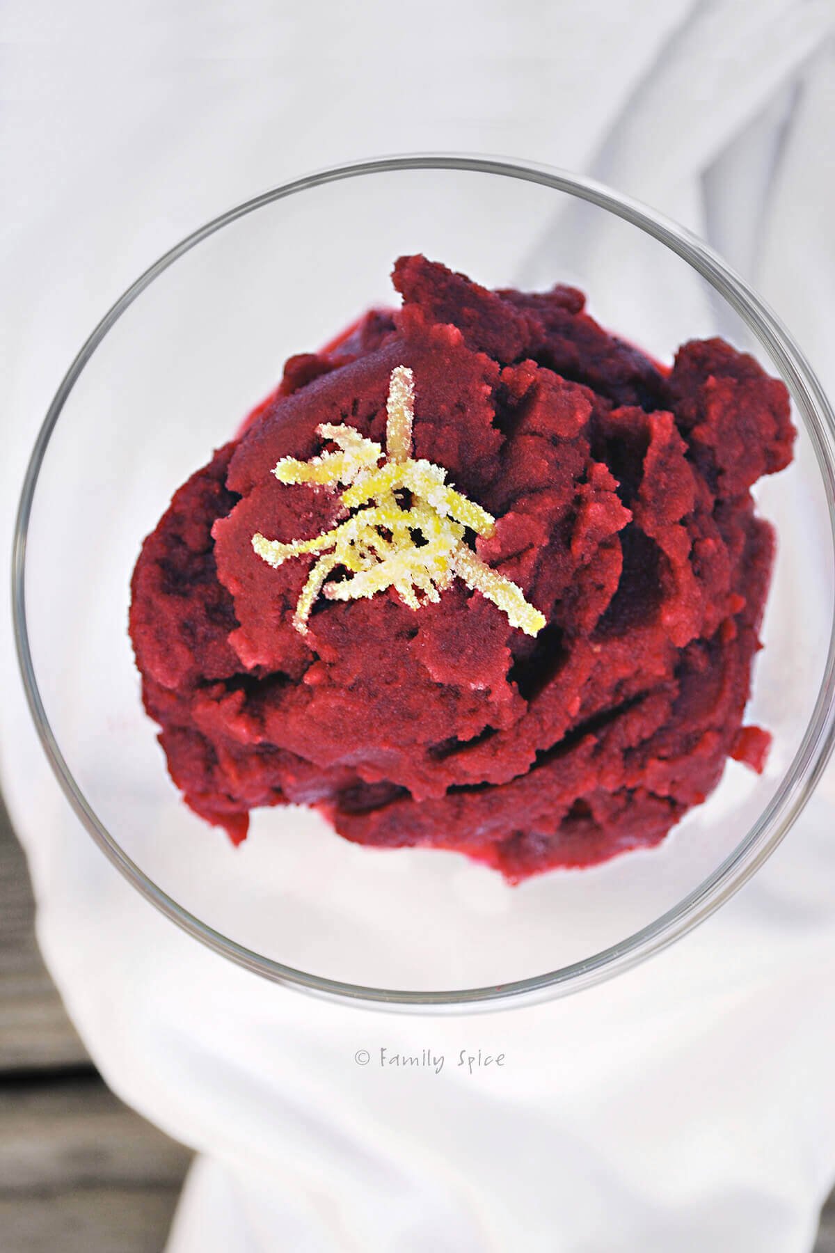 A glass bowl with pomegranate granita topped with lemon peel