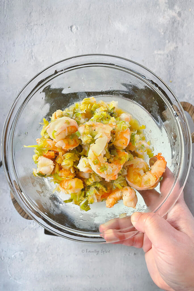 A glass bowl with sautéed leeks and cooked shrimp in it