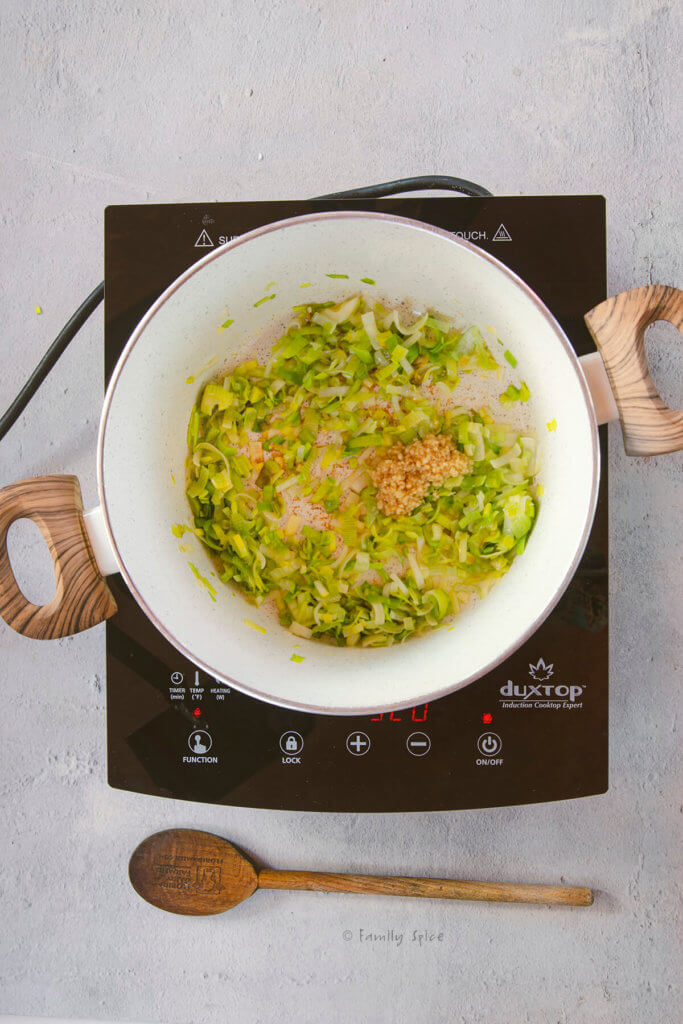 A pot on a cooktop with sautéed chopped leeks and chopped garlic