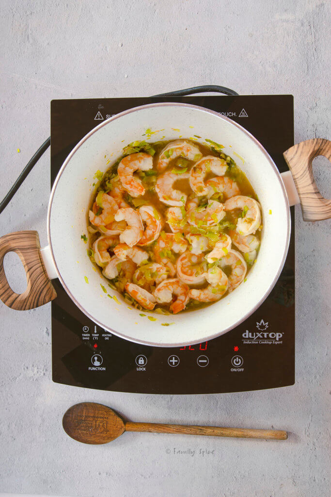 A pot on a cooktop with sautéed chopped leeks, shrimp, cognac and cooking sherry in it